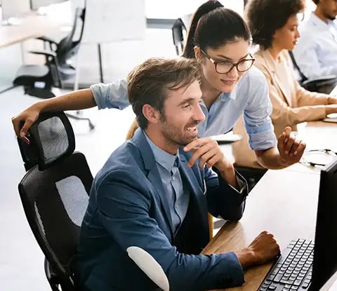 A group of professionals collaborate in a modern office, focused on their computer screens, with friendly interaction visible.