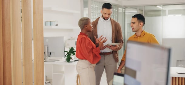 Three colleagues engage in a lively discussion in a modern office, surrounded by plants and contemporary décor.