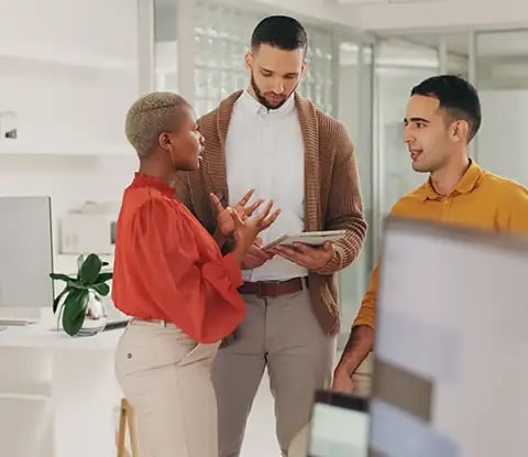 Trois collègues se livrent à une discussion animée sur l'accompagnement et la formation en marketing numérique dans un bureau moderne, entouré de plantes et d'un décor contemporain.