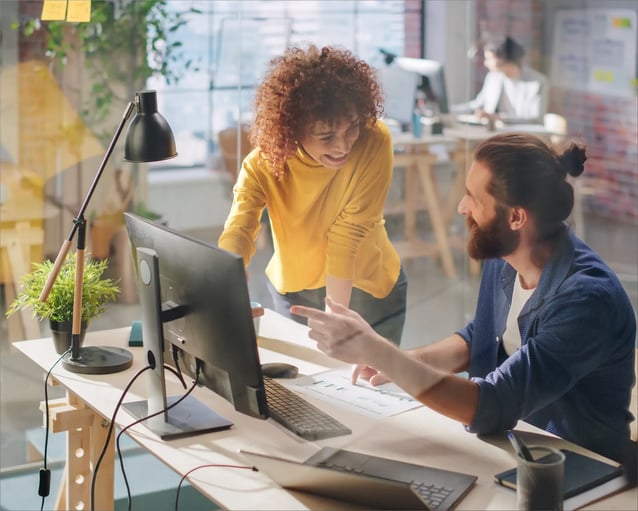 Two colleagues collaborate in a modern workspace, discussing a document amidst plants and office equipment.