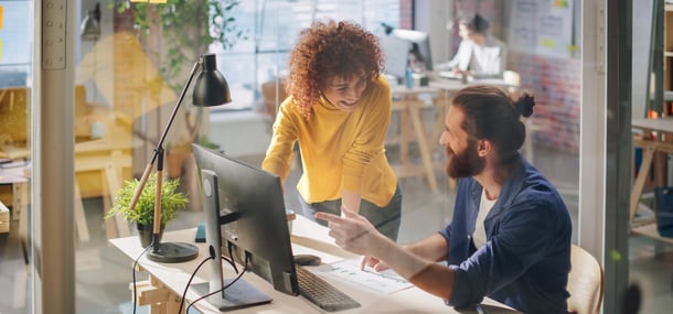 Two colleagues collaborate in a modern workspace, discussing a document amidst plants and office equipment.
