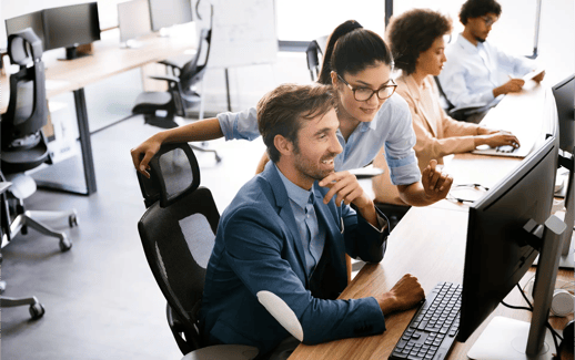 A group of professionals collaborates in a modern office, focused on their computer screens, with a friendly interaction visible.