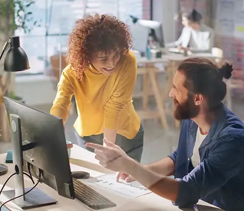 Deux collègues collaborent dans un espace de travail moderne, discutant d'un document d'optimisation de CRM au milieu de plantes et d'équipements de bureau.