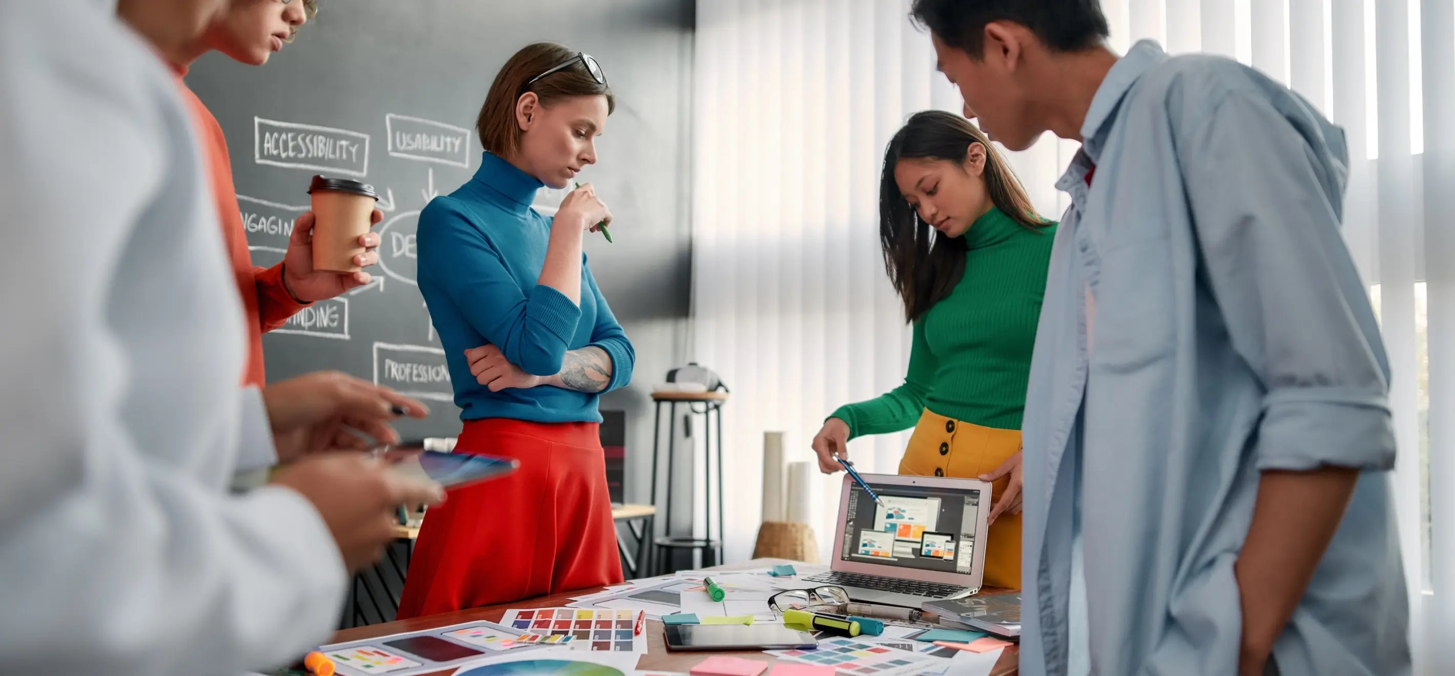 A group of professionals collaborate around a table filled with design materials, color swatches and digital devices in a bright office.