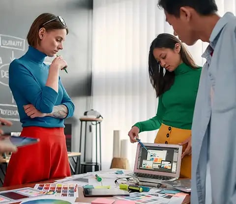 Un groupe de professionnels collabore autour d'une table remplie de matériel de conception, d'échantillons de couleurs et d'appareils numériques dans un bureau lumineux.