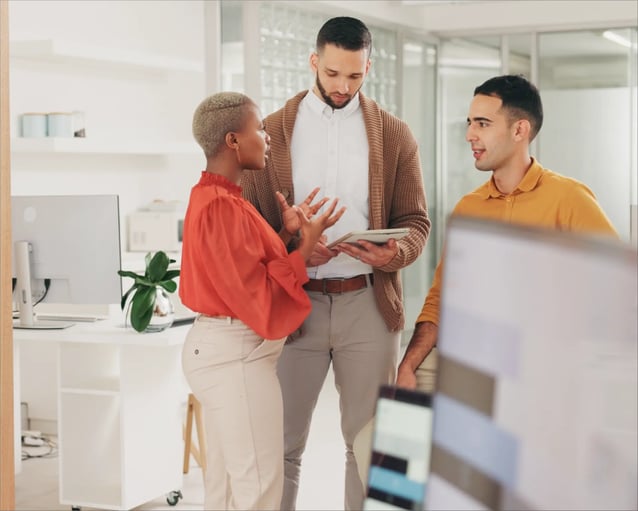 Three colleagues engage in a lively discussion in a modern office, surrounded by plants and contemporary décor.