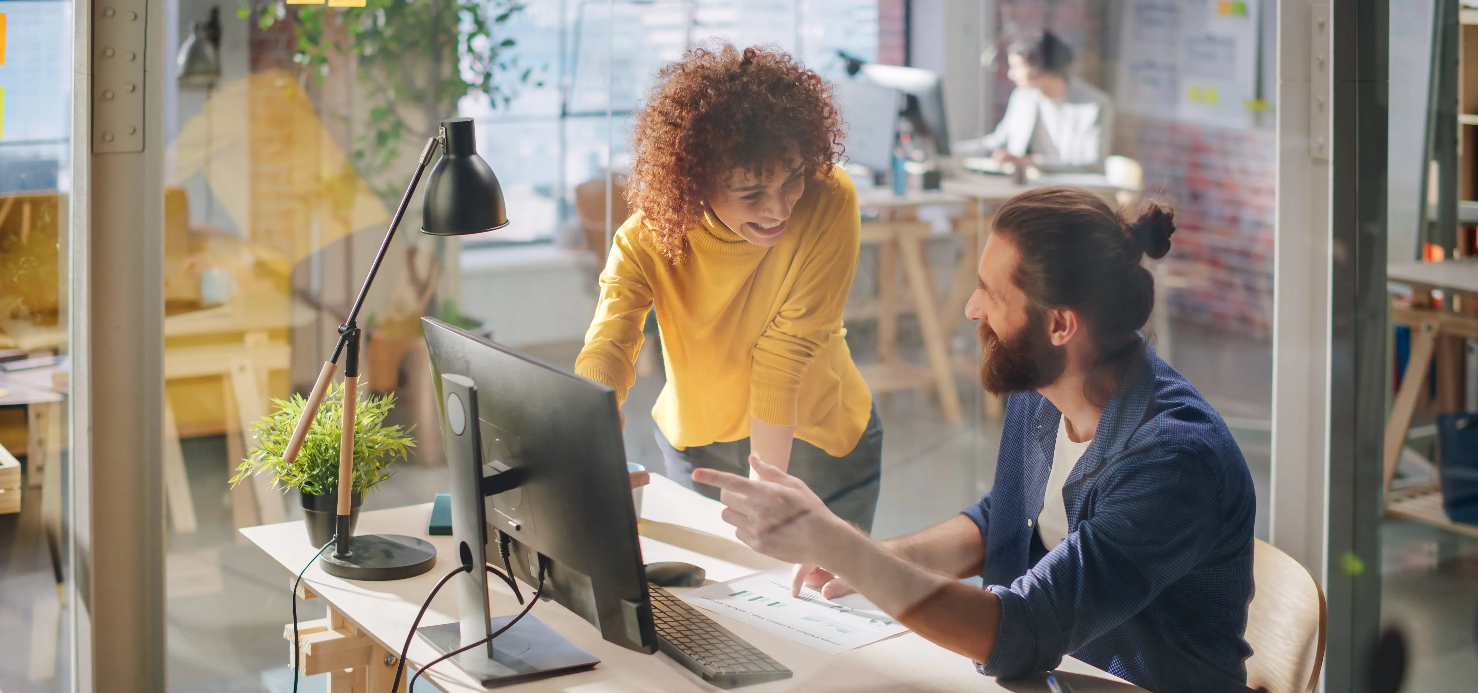 Deux collègues collaborent dans un espace de travail moderne, discutant d'un document d'optimisation de CRM au milieu de plantes et d'équipements de bureau.