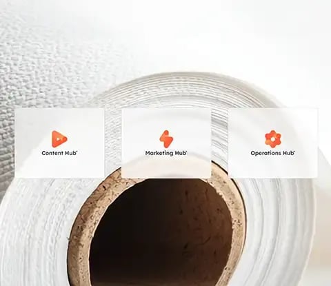 Three HubSpot hub icons: Content Hub, Marketing Hub and Operations Hub are displayed on a textured white paper background.