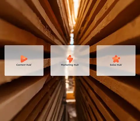 Trois icônes HubSpot : Content Hub, Marketing Hub et Sales Hub sur un fond flou de planches de bois empilées.