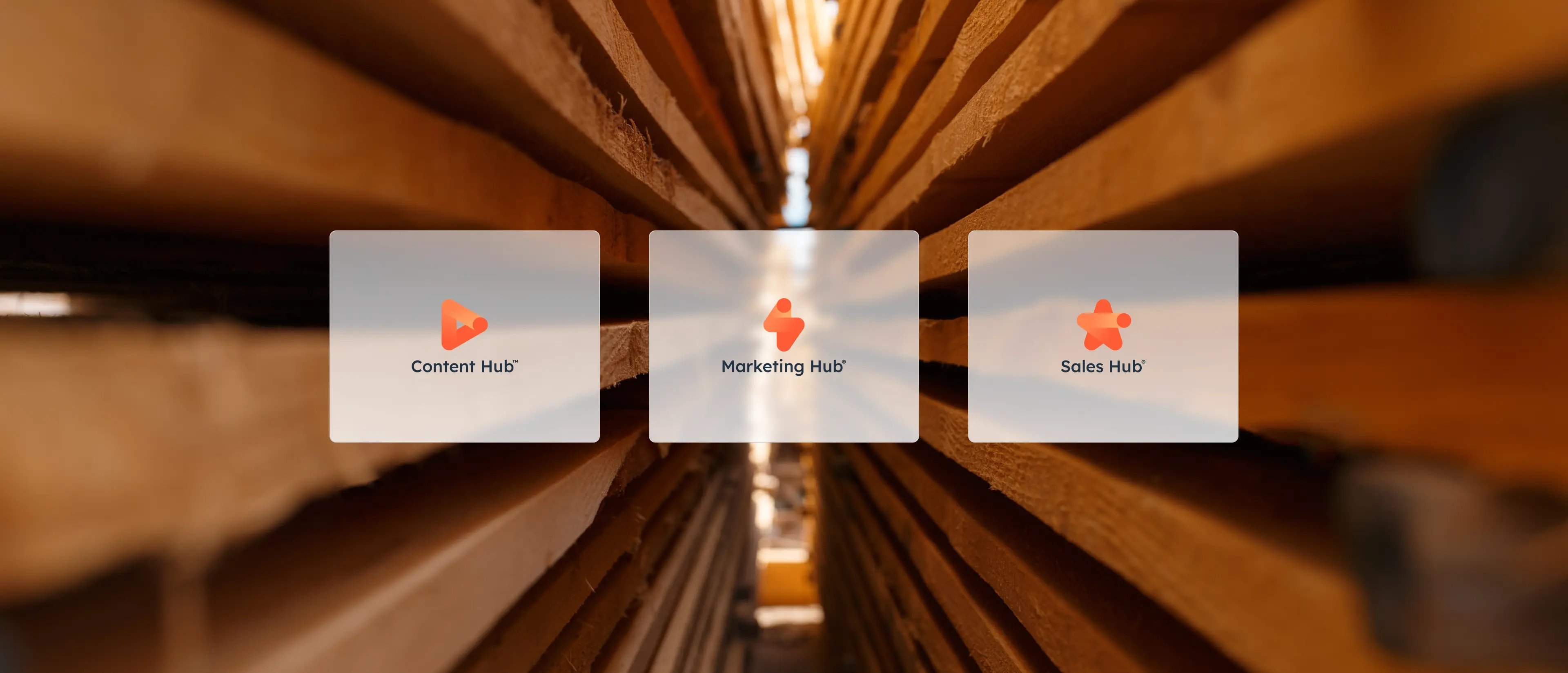 Trois icônes HubSpot : Content Hub, Marketing Hub et Sales Hub sur un fond flou de planches de bois empilées.