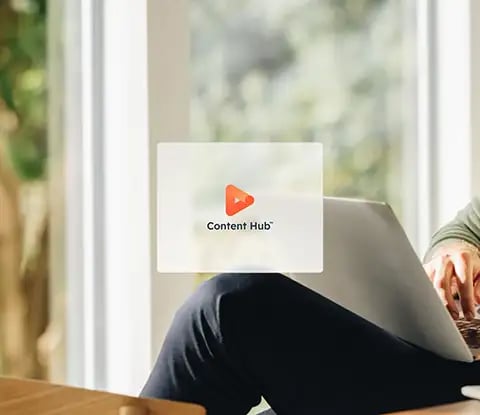 Une icônes de hub de HubSpot : Content Hub, est affichée sur une image d'une personne assise à une table en bois, travaillant sur un ordinateur portable entourée de verdure et de lumière naturelle.